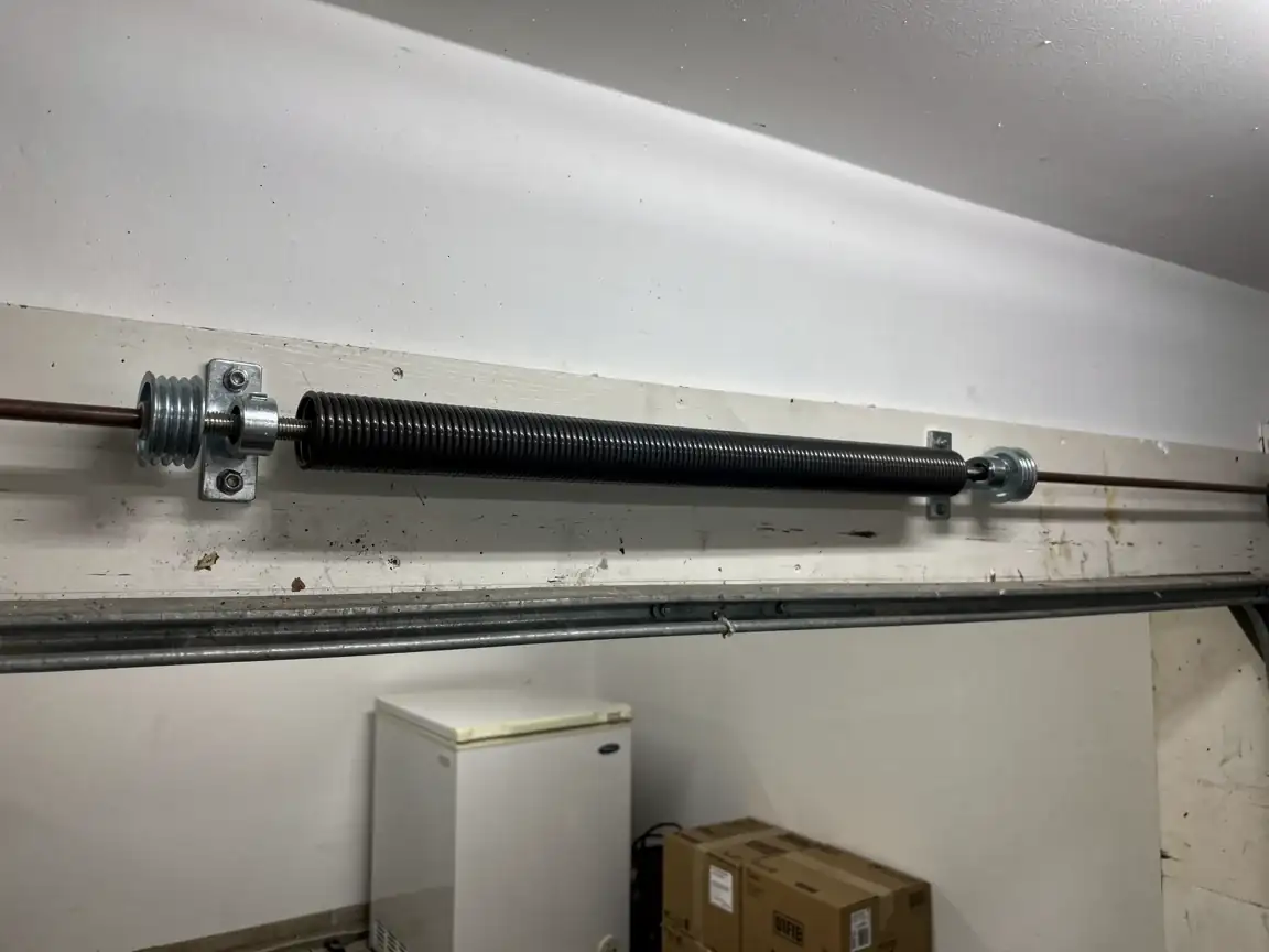 A black torsion spring is mounted above a garage door.